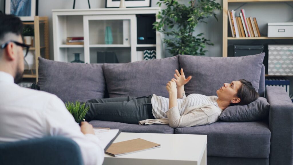 A woman in therapy, speaking with a psychologist while lying on a sofa, indoors.